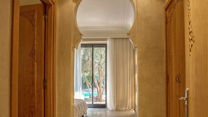 A hallway with a marble floor, wooden doors with intricate carvings, and a large arched doorway leading to a room with a view of trees and a pool. - Villa Touareg Domaine des Kasbahs (Marrakech)