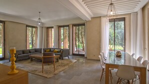 Ein großzügiger Wohnbereich mit Sofa, Couchtisch und Esstisch mit Stühlen. Große Fenster bieten Blick ins Freie.