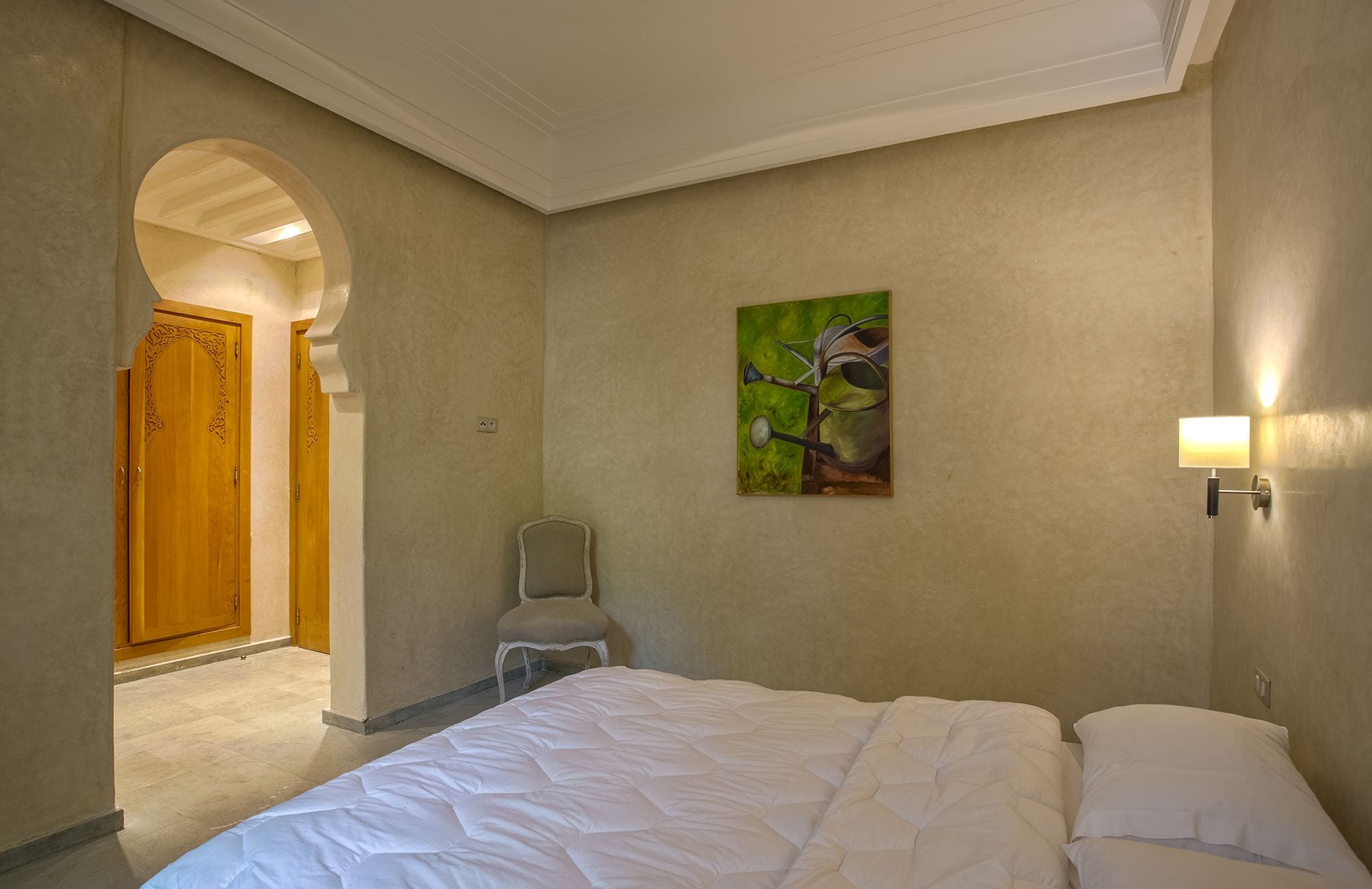 Ein Hotelzimmer mit Bett, Sessel, Gemälde und Tür.