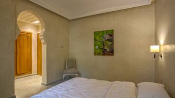 Ein Hotelzimmer mit Bett, Sessel, Gemälde und Tür.
