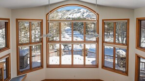 A dining room with a large wooden table and multiple chairs, large windows with a view of a snowy mountain landscape.