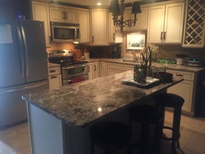 A kitchen with granite countertops, stainless steel appliances, and white cabinetry. - Not Your Ordinary Beach Rental (St Augustine)