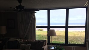 Sala de estar con un amplio ventanal que da a una zona verde. Se aprecia un sofá, una mesa de centro y una lámpara.