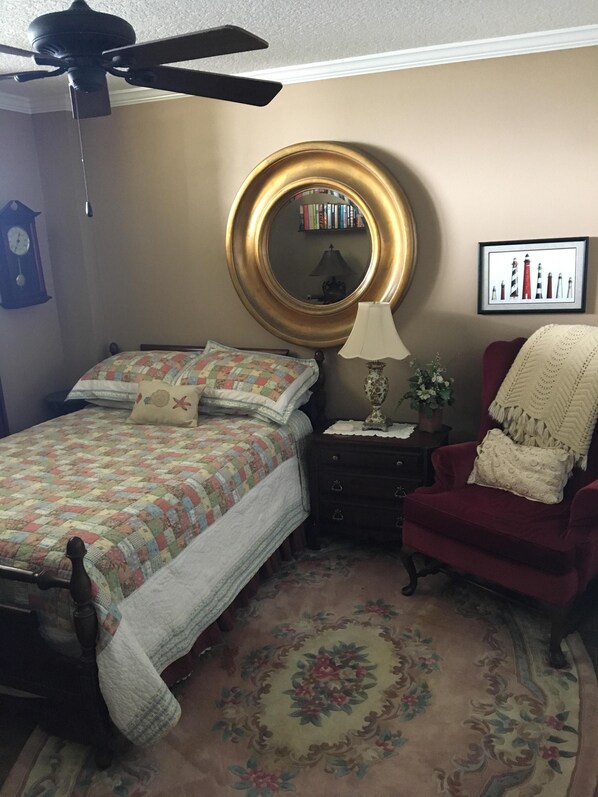 A bedroom with a bed, a red armchair, a round mirror, a lamp, a clock, and a framed picture on the wall. - Not Your Ordinary Beach Rental (St Augustine)