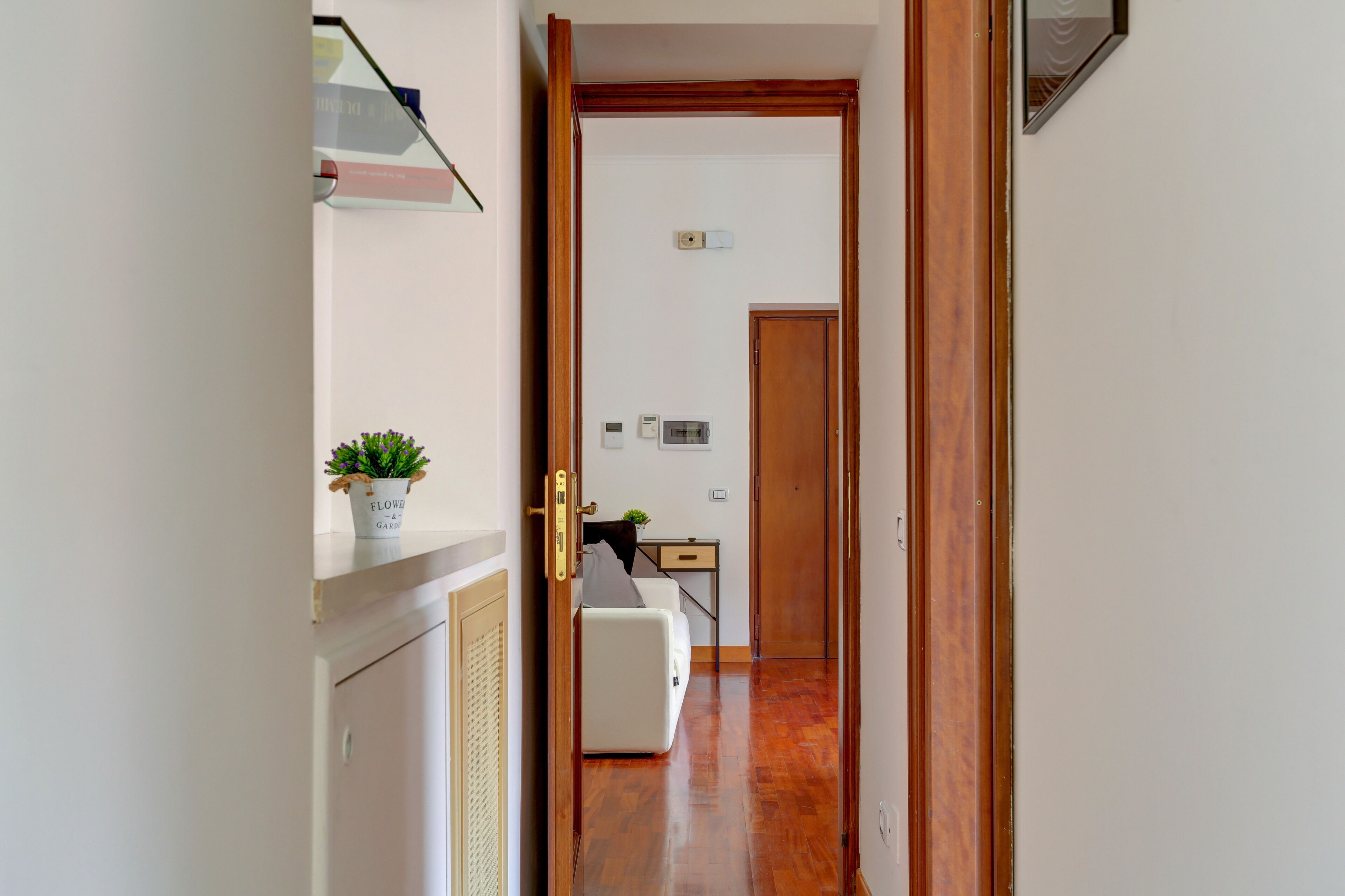 A hallway with a white sofa, a small table with a plant, and a wooden door leading to another room.