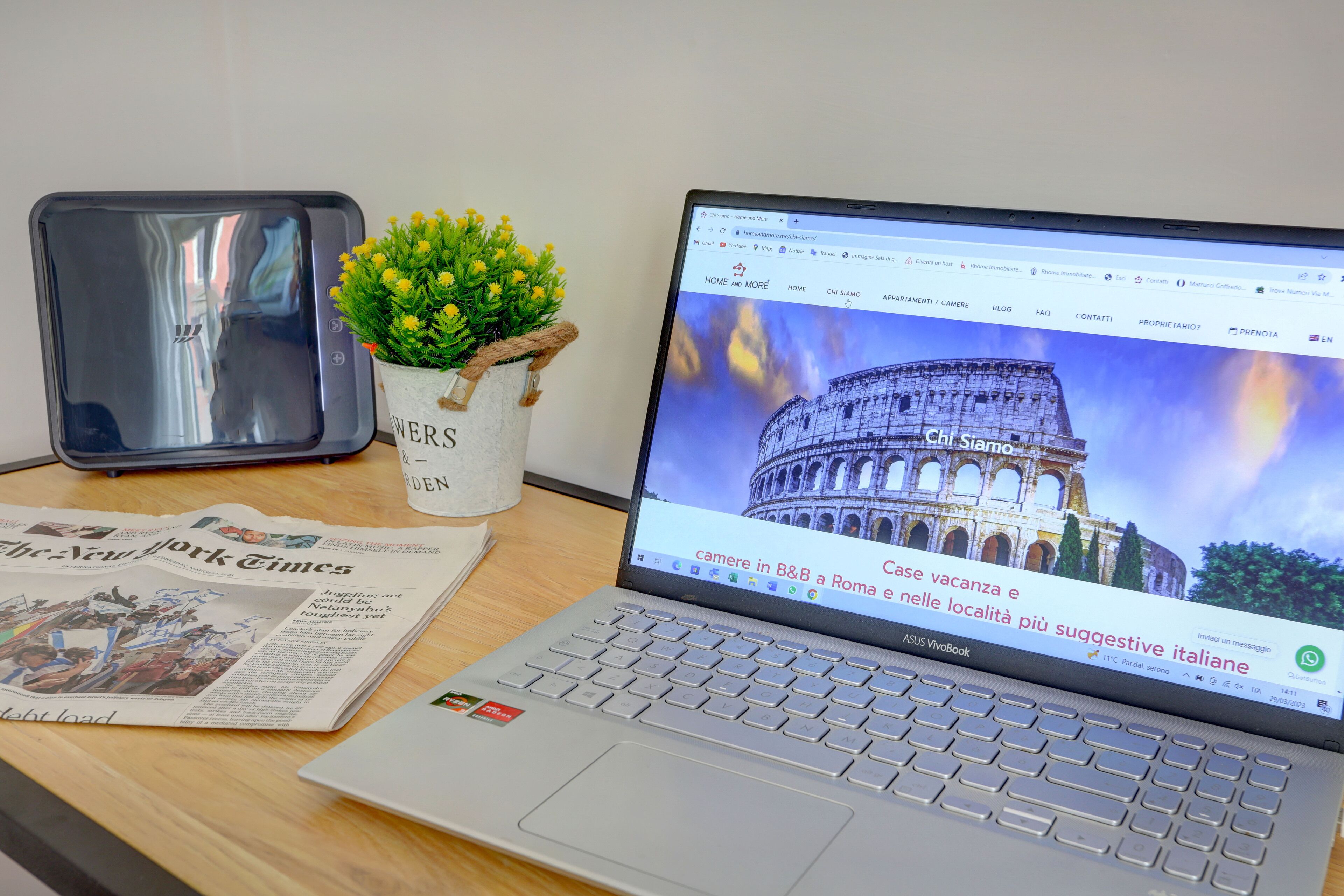 A laptop on a desk with a newspaper, a plant, and a smartphone.
