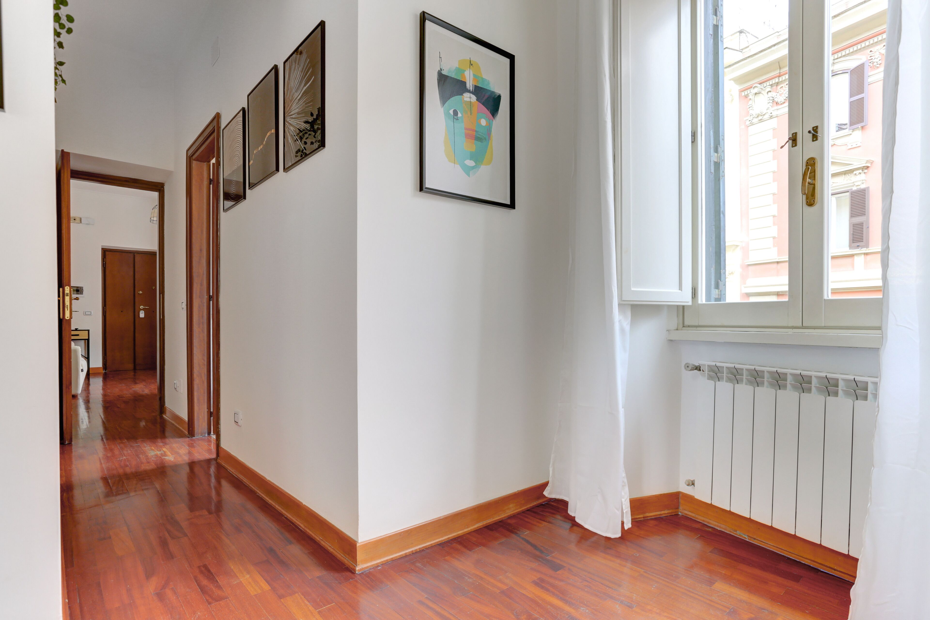 A hallway with wooden flooring, a radiator, and a window with a curtain.