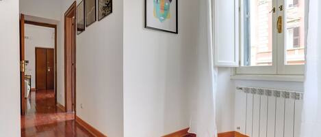 A hallway with wooden flooring, a radiator, and a window with a curtain.