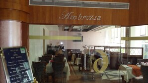 A hotel lobby with a wooden ceiling and a sign reading "Ambrozia". Tables and chairs are arranged for dining, and a signboard lists hotel amenities and events. - Hotel The Amaris (Rishikesh)