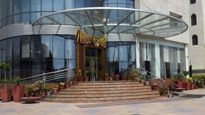 A modern building with a curved glass entrance, a set of outdoor stairs, and potted plants. - Hotel The Amaris (Rishikesh)