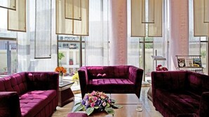 A spacious room with large windows, a plush purple sofa, and a coffee table with a floral arrangement. - Hotel The Amaris (Rishikesh)
