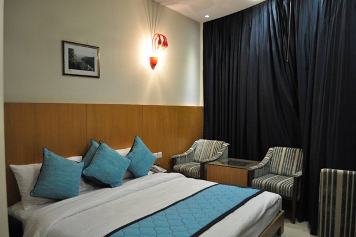 A hotel room with a large bed, two striped armchairs, a small table, a wall-mounted light, and a framed picture on the wall.