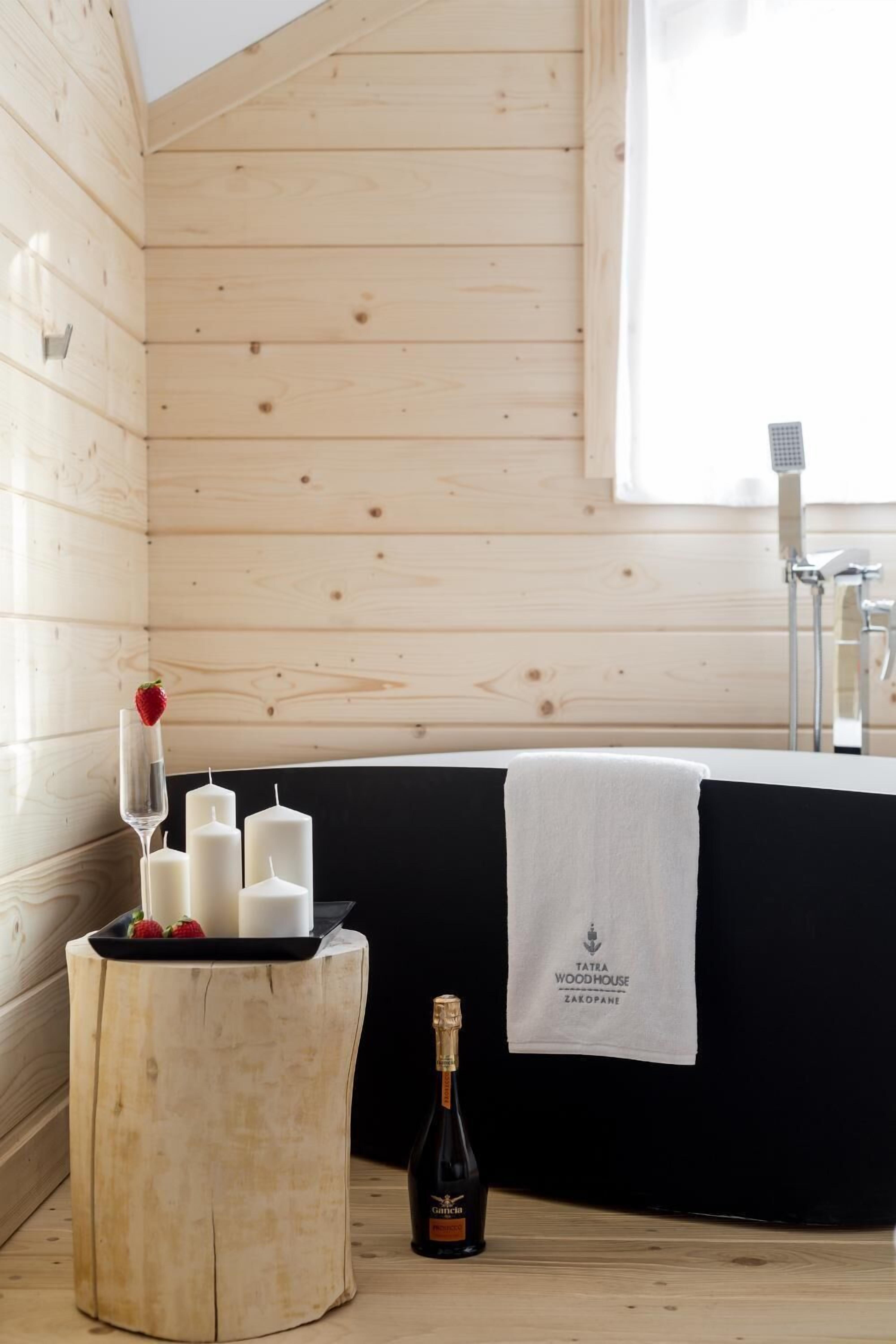 Interno di una baita in legno con una vasca da bagno, candele, una bottiglia di champagne e un vassoio con fragole.