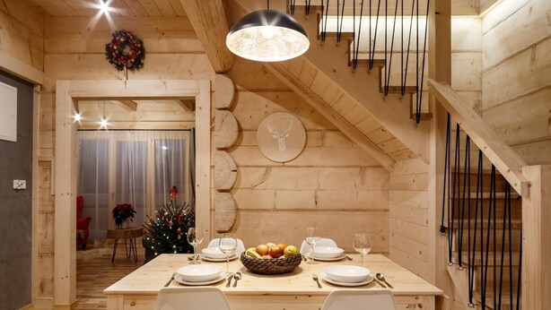 A cozy wooden dining area with a table set for two, a Christmas tree, and a staircase with wooden railings. - Tatra Wood House (Zakopane)