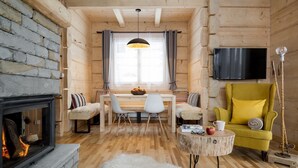 A cozy log cabin interior with a fireplace, a dining table with chairs, a yellow armchair, and a television mounted on the wall. - Tatra Wood House (Zakopane)
