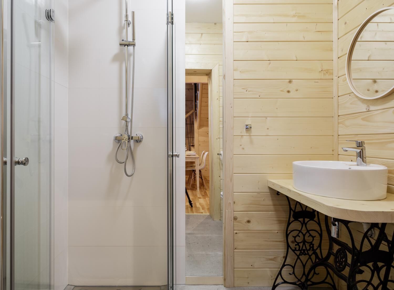 Un baño con cabina de ducha de vidrio, un lavamanos blanco y un espejo redondo, y paneles de madera.