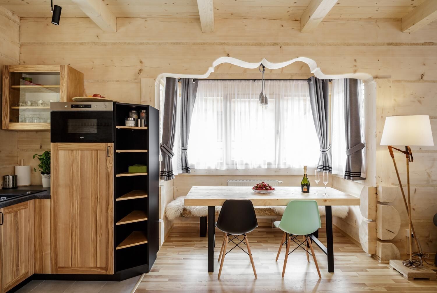 A cozy wooden interior with a dining area, a kitchen with a microwave, and a lamp.