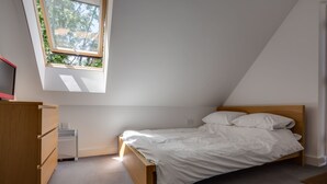 A bedroom with a sloped ceiling, a single bed, a wooden wardrobe, and a radiator. - The Annexe (Cheltenham)