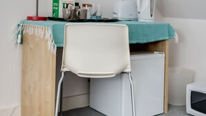 A small, compact room with a desk, a chair, a red desk lamp, a white kettle, and a microwave. - The Annexe (Cheltenham)