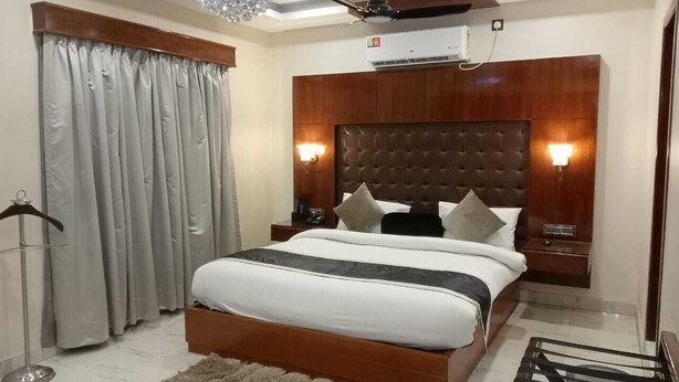 A bedroom with a large bed, wooden headboard, two bedside tables, a ceiling fan, and a chandelier. - Hotel Baidyanath (Deoghar)