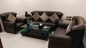 A living room with a brown leather sofa set, a glass coffee table, and a small side table. - Hotel Baidyanath (Deoghar)