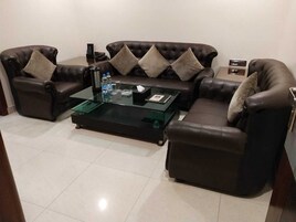 Un salón con un sofá de cuero marrón, una mesa de centro de vidrio y una mesita auxiliar.