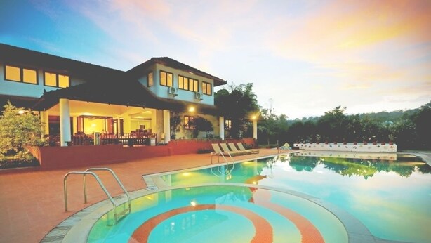 Un hotel con piscina, un espacio exterior cubierto y una casa grande con múltiples ventanas.