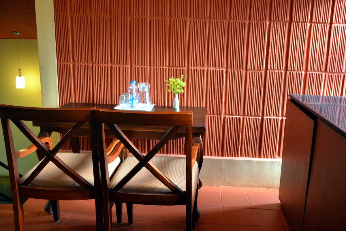 A dining area with a wooden table and chairs, a vase with a plant, and a textured wall in the background.
