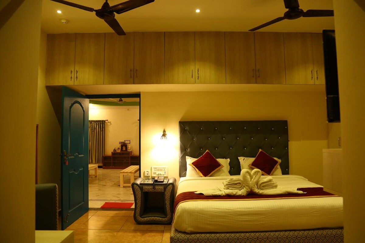 Una habitación de hotel con una cama, una mesita de noche, un ventilador de techo y armarios de madera sobre la cama.