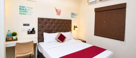 A hotel room with a bed, a desk, a chair, an air conditioner, and motivational wall stickers.