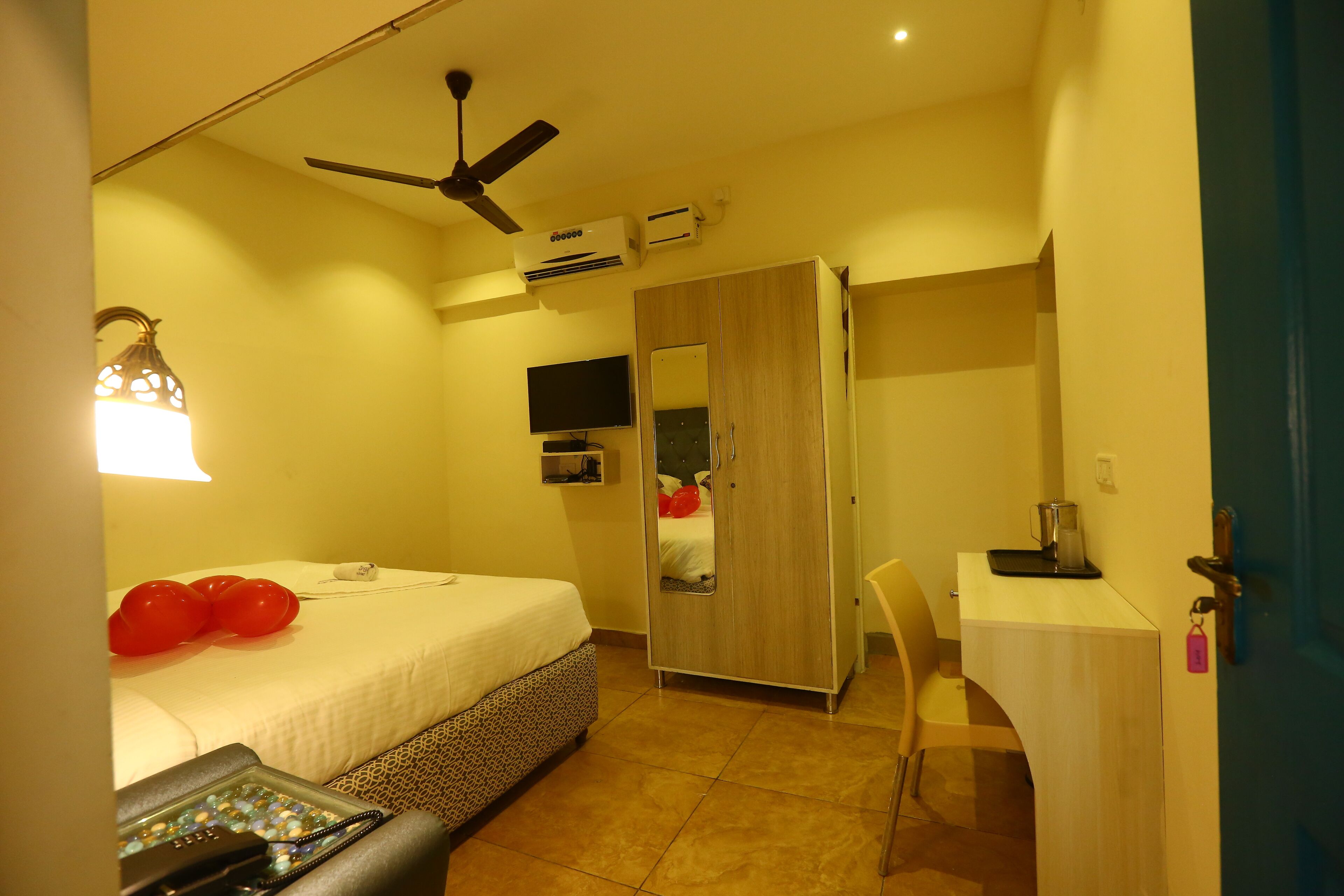Ein Hotelzimmer mit Bett, Schreibtisch, Kleiderschrank, Deckenventilator und Klimaanlage.
