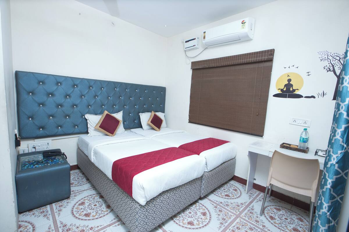 Een slaapkamer met een gestoffeerd hoofdeinde, een bed met wit en rode beddengoed, een bureau en een vloer met een patroon.