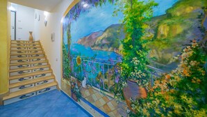 A staircase with ornate balusters and a mural depicting a coastal landscape with cliffs and vegetation. - B&B Il Girasole (Agerola)