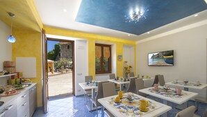 A dining area with tables set for service, a view of the outdoors, and a painting on the wall. - B&B Il Girasole (Agerola)