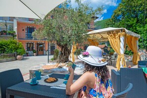 Un espacio al aire libre con mesas y sillas, un árbol y un edificio en el fondo.