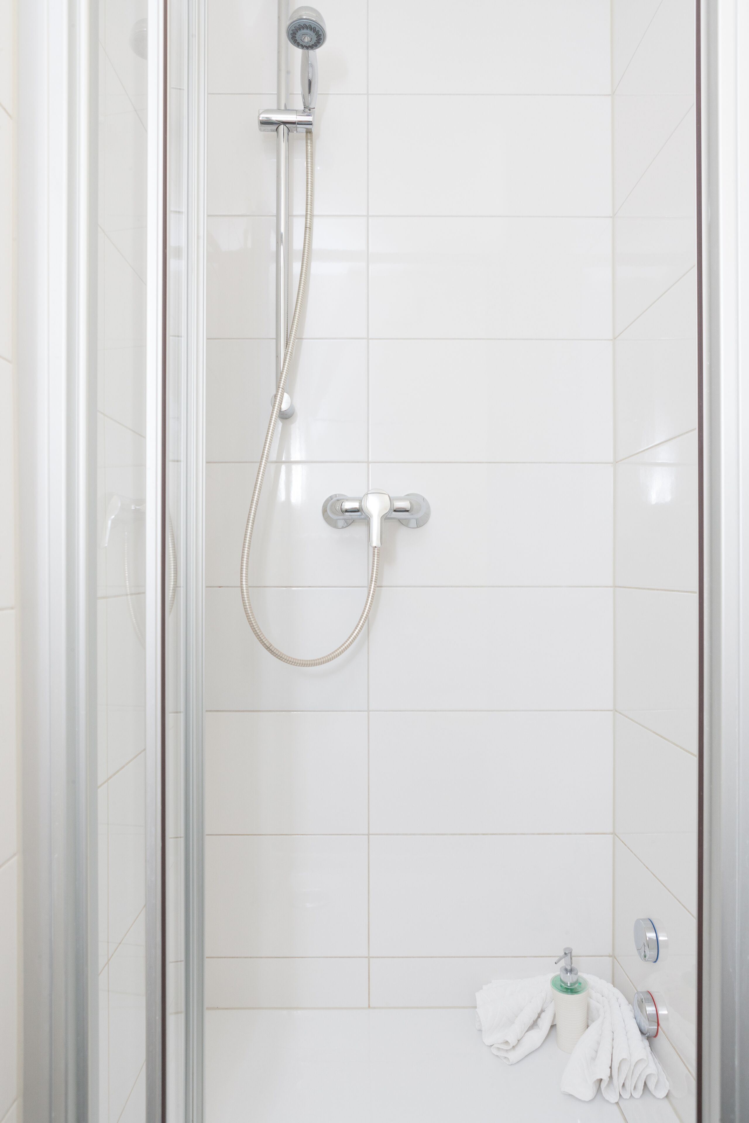 Een douchecabine met glazen wanden, een handdouche en een muurbevestigde kraan.