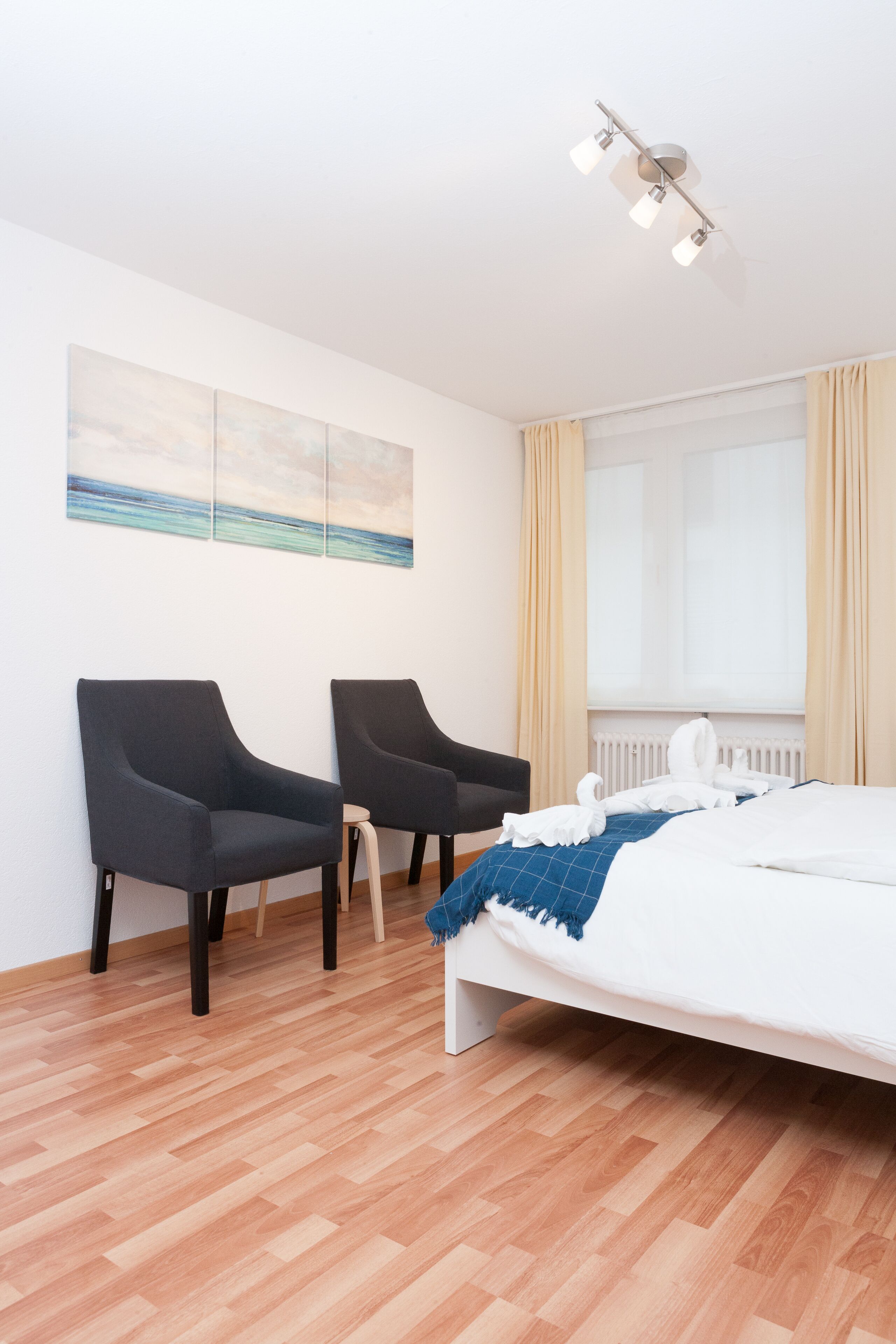 Ein Hotelzimmer mit einem Bett, zwei Sesseln, einem Gemälde an der Wand und einem Fenster mit Vorhängen.