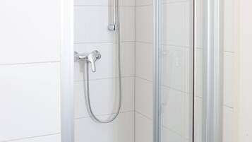 Una ducha con cerramiento de vidrio, un cabezal de ducha de mano y un grifo empotrado en la pared.