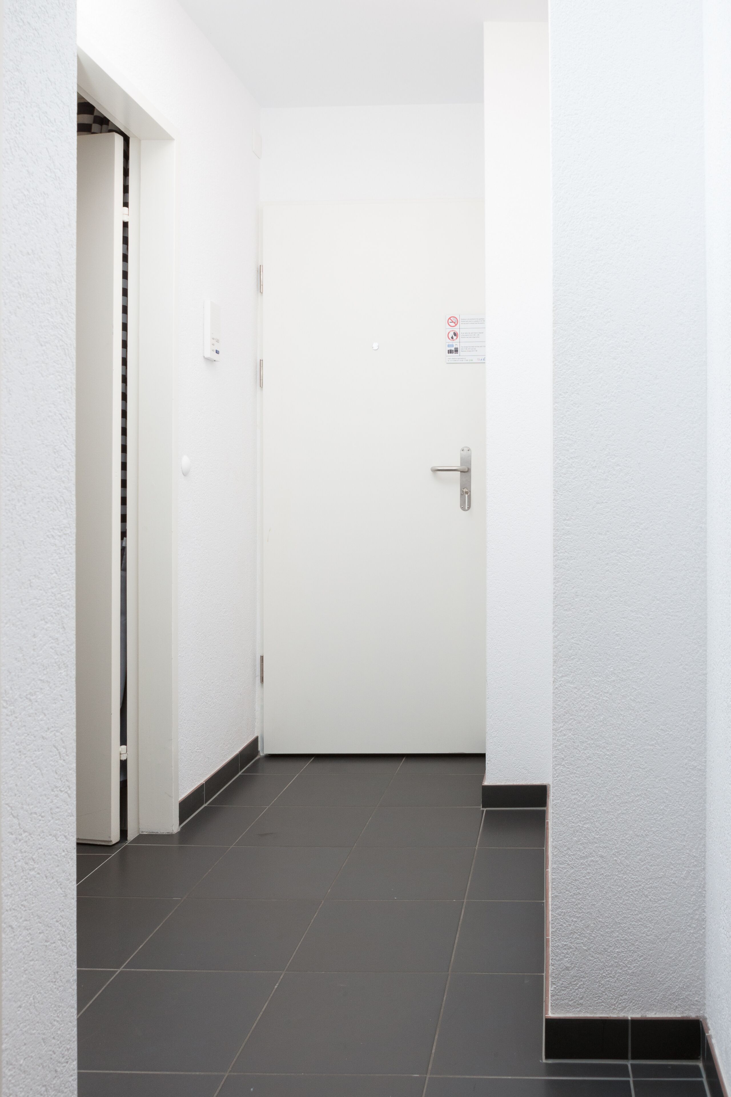 A hallway with a white door, a doorbell, and a wall-mounted light switch.