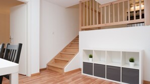 A modern interior with a wooden staircase, a dining area with chairs, and a white console unit with shelves. - Galaxy Apartments (Lucerne)