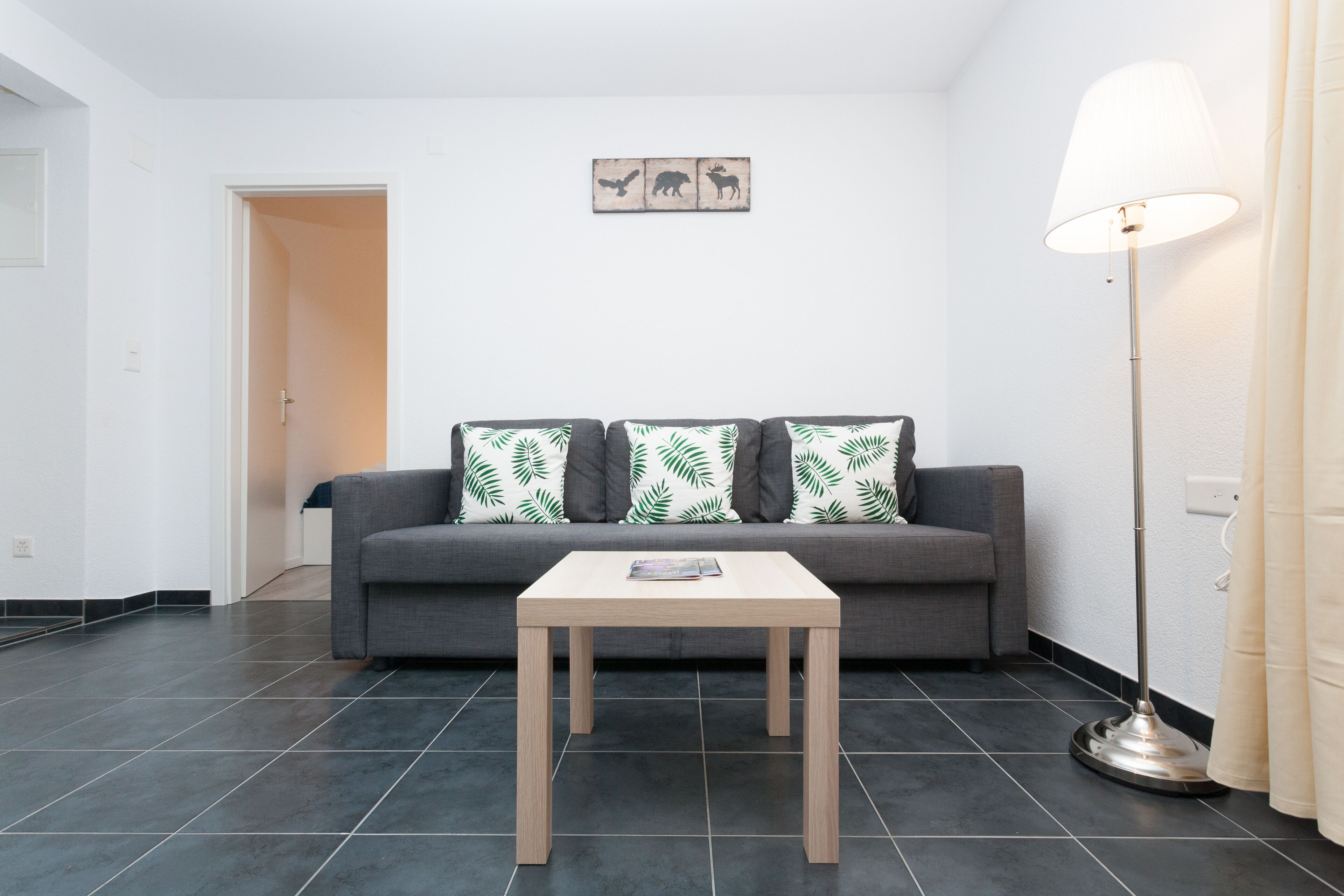 Ein Wohnzimmer mit grauem Sofa, einem Holztisch und einer Stehlampe.