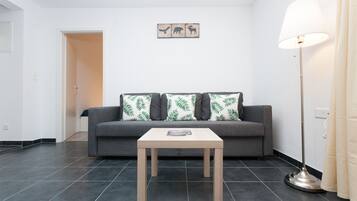 Ein Wohnzimmer mit grauem Sofa, einem Holztisch und einer Stehlampe.