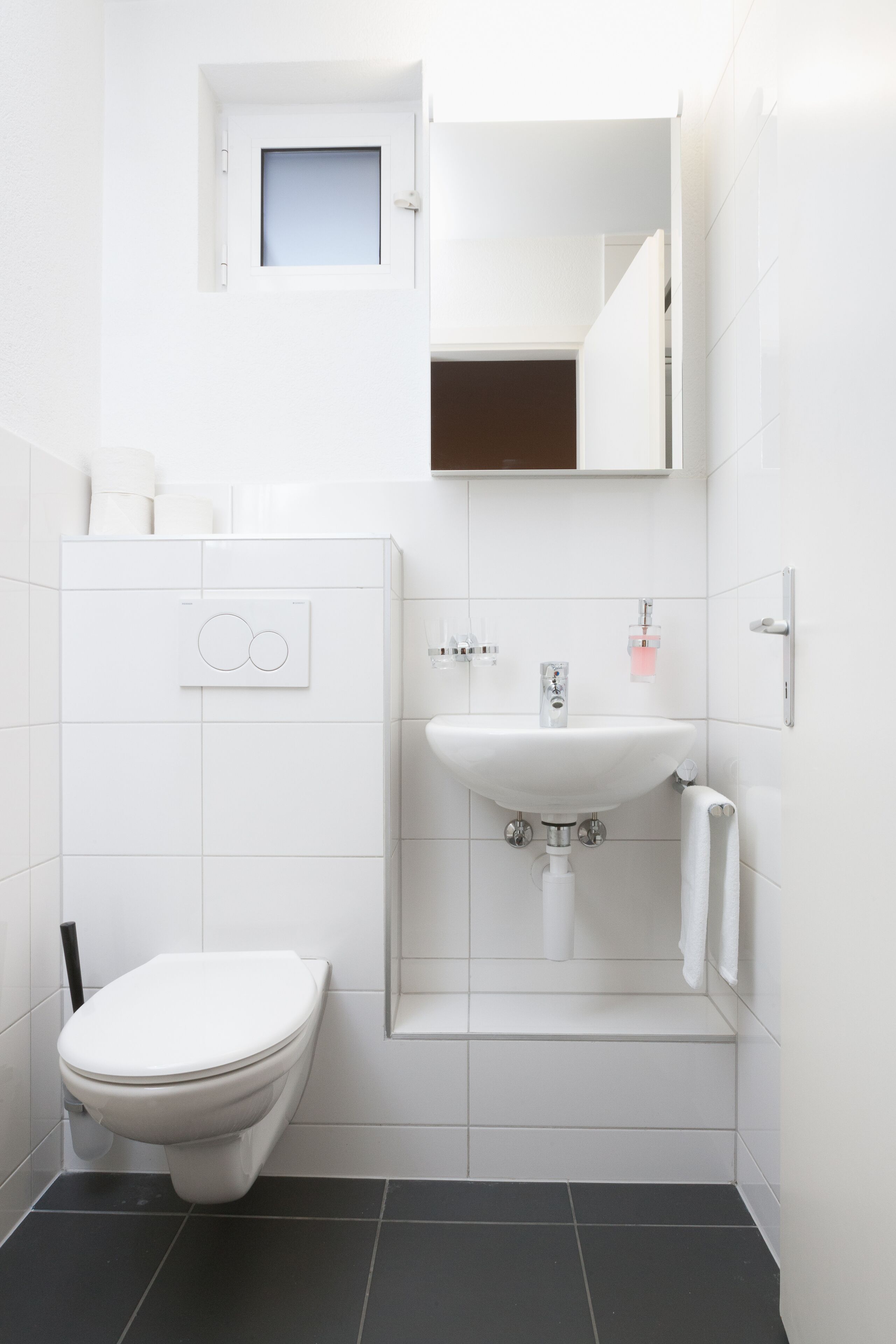 Ein modernes Badezimmer mit Toilette, Waschbecken und einem kleinen Fenster über dem Waschbecken.