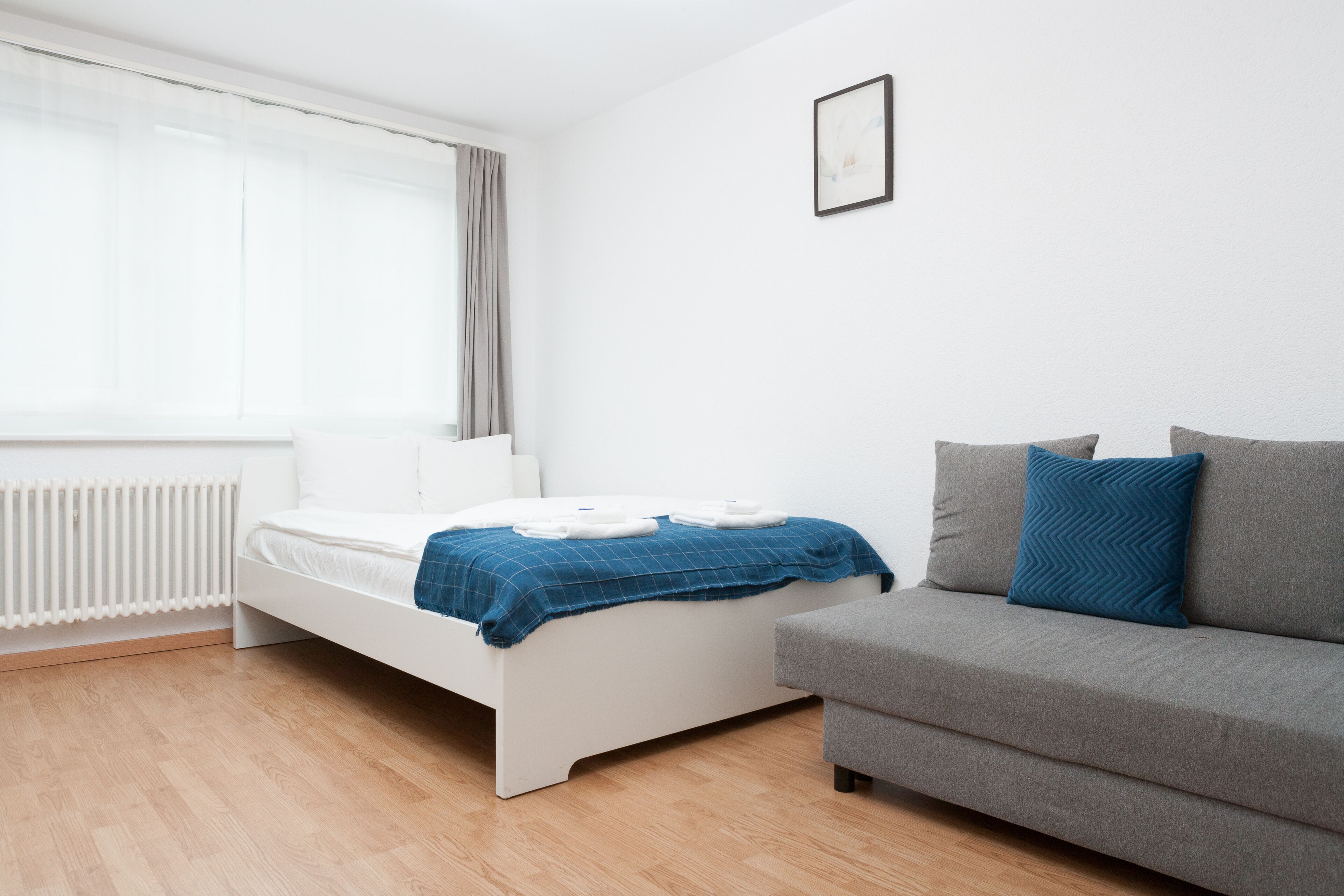 A modern bedroom with a white bed, a grey sofa, and a window with sheer curtains.