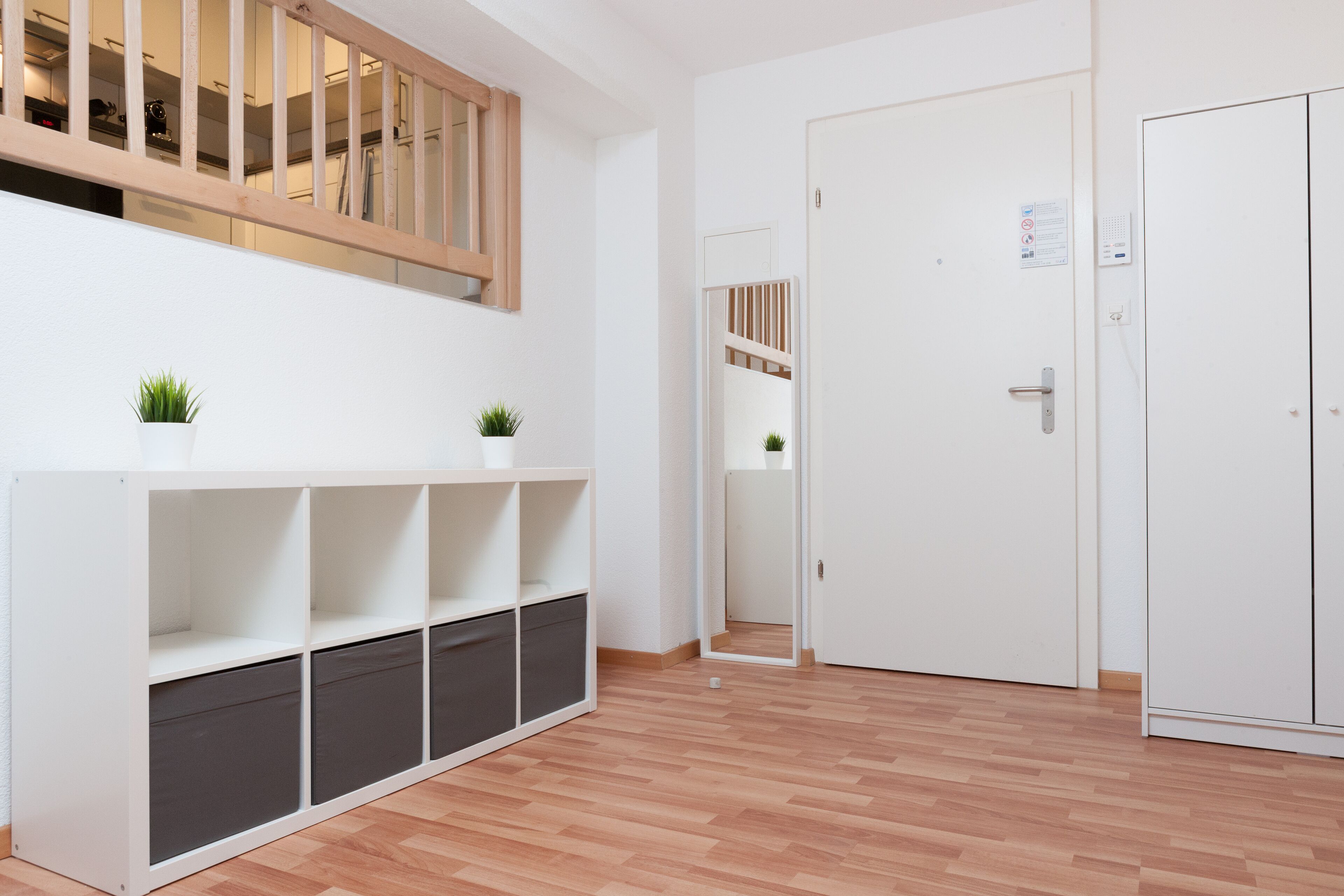 Una habitación con piso de madera, paredes blancas, un armario blanco y una estantería blanca con dos plantas en macetas.