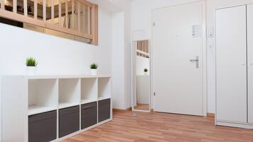 Una habitación con piso de madera, paredes blancas, un armario blanco y una estantería blanca con dos plantas en macetas.