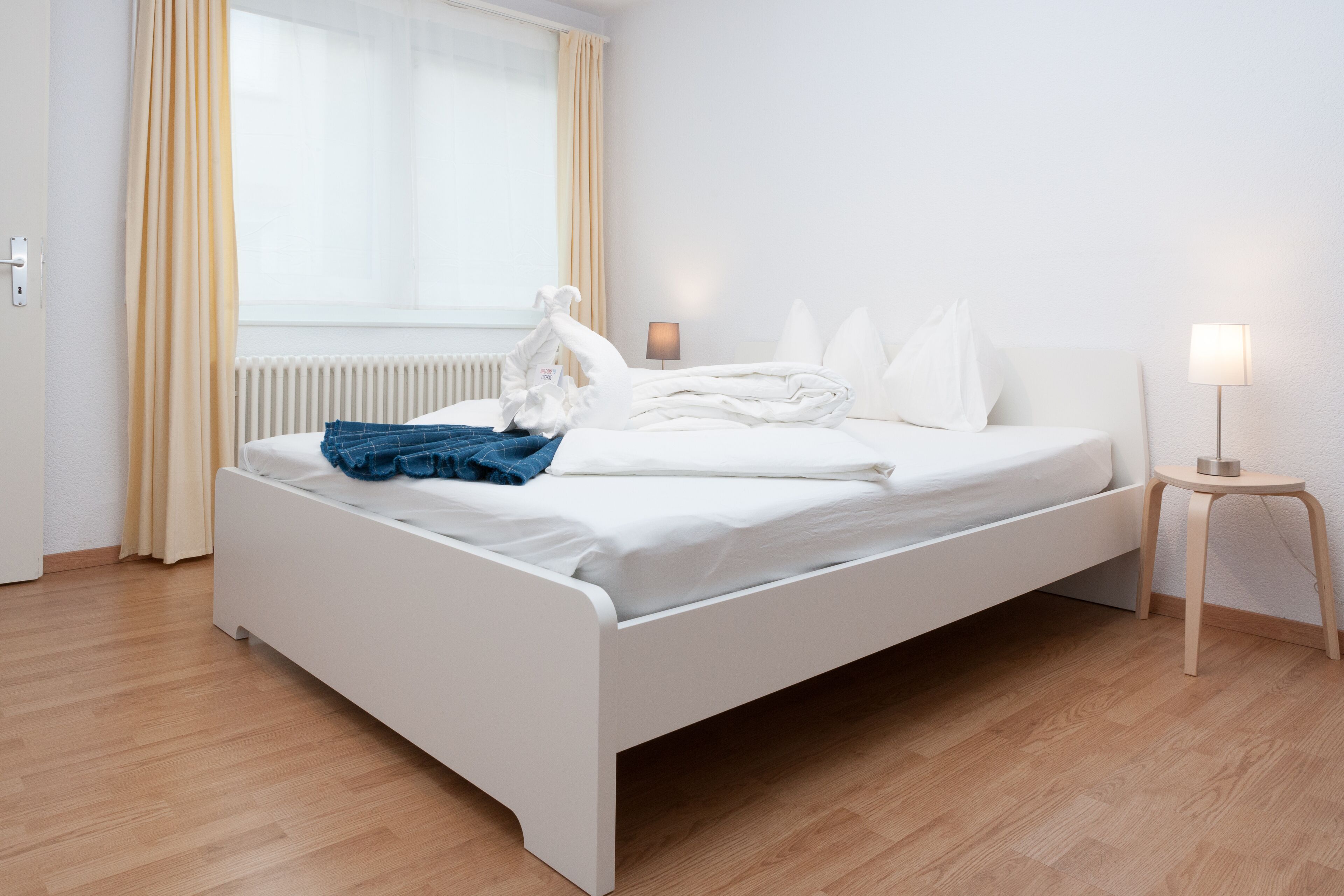 Ein modernes Hotelzimmer mit einem weißen Bett, Holzboden und einem Fenster mit Vorhängen.