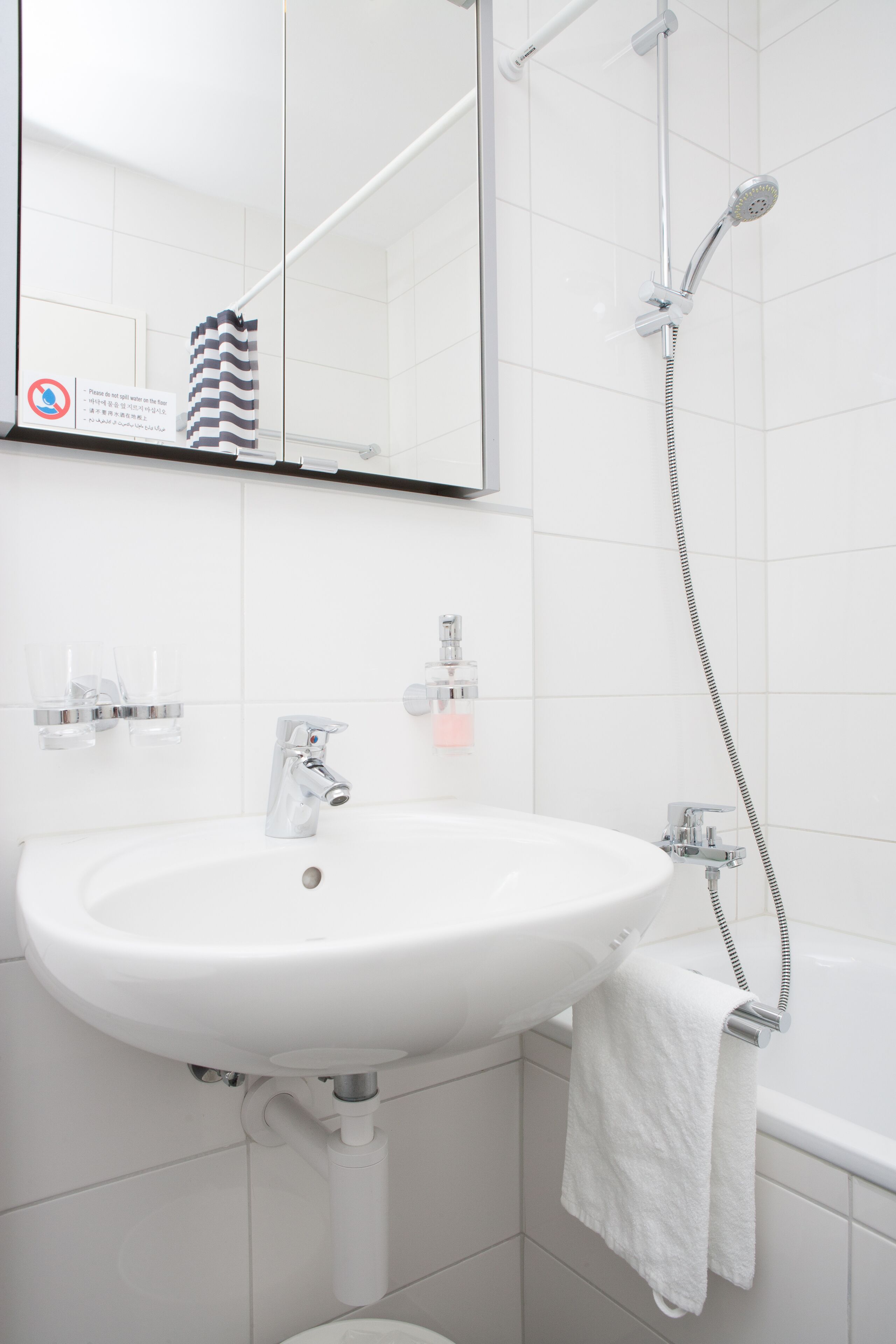 Une salle de bain avec un lavabo blanc, un miroir, une douche et une serviette accrochée au mur.