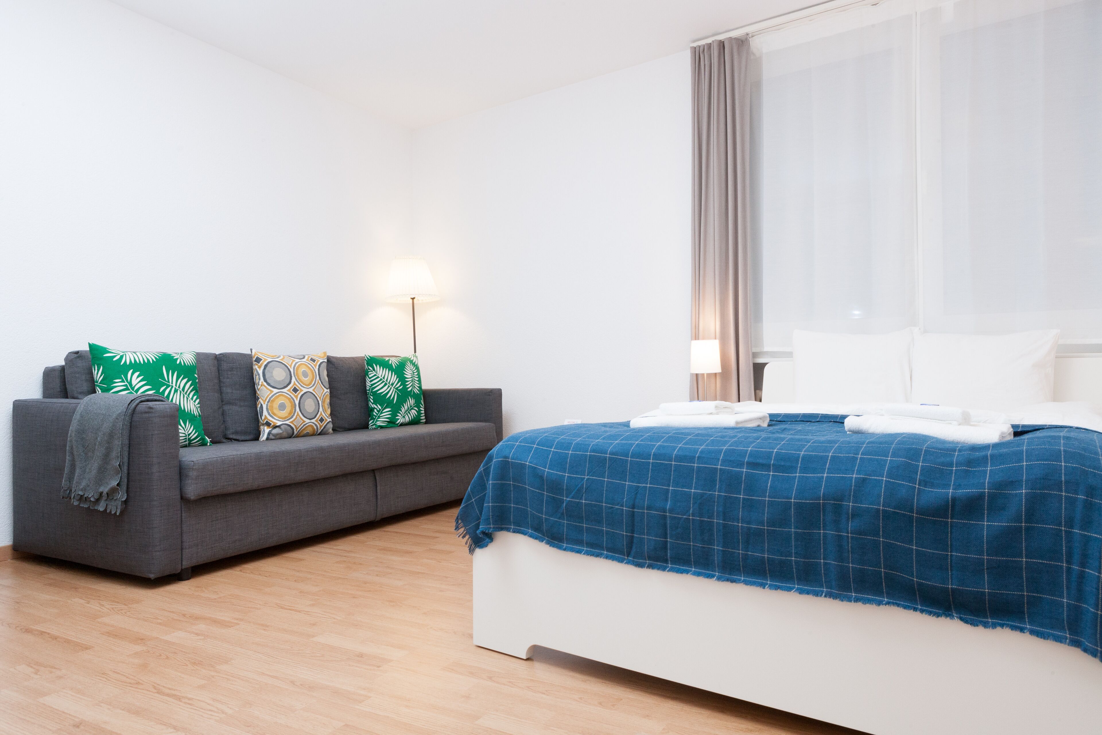 Ein Schlafzimmer mit einem Bett, einem grauen Sofa und einer Stehlampe.
