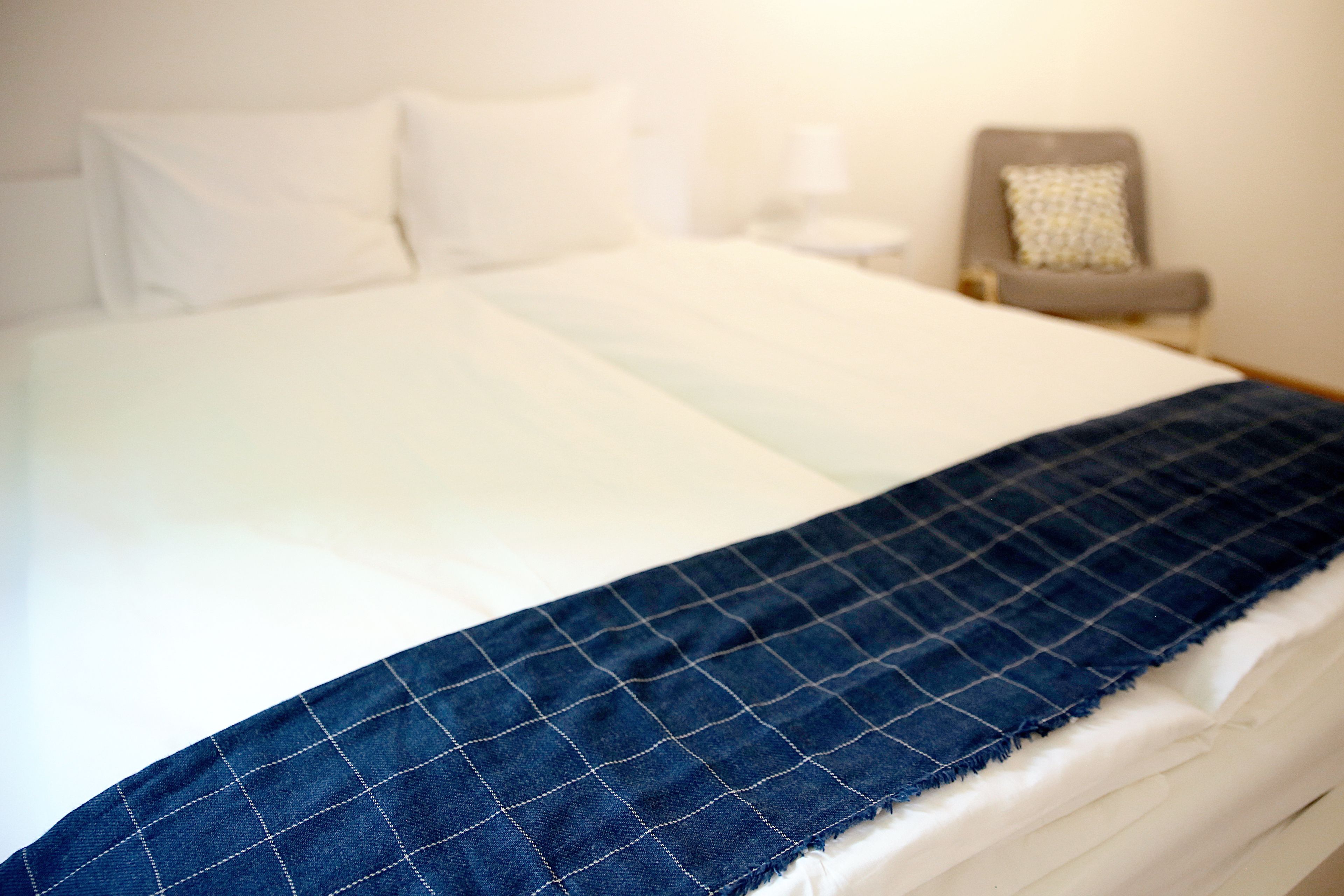 A neatly made bed with a white duvet and a blue quilted blanket.